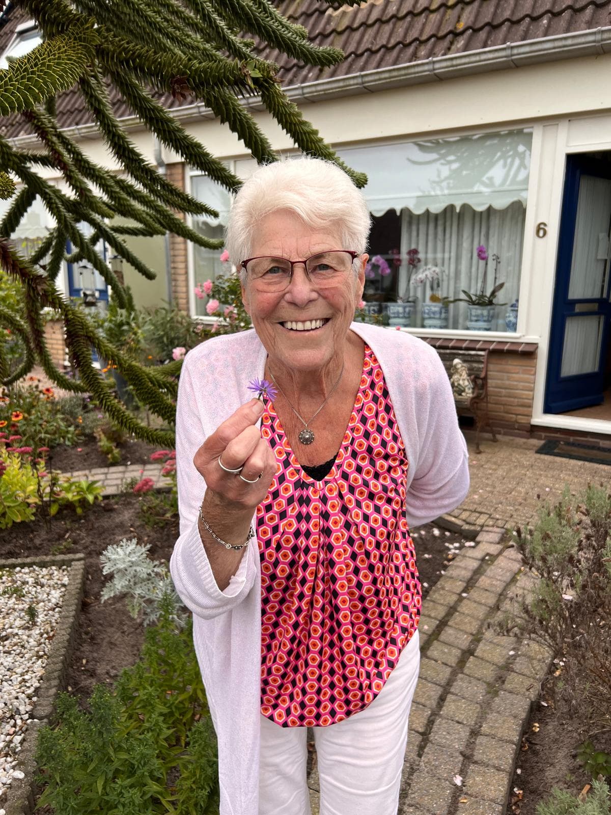 Oma, het boegbeeld van TOEK, met een bloemetje in haar hand voor haar huis